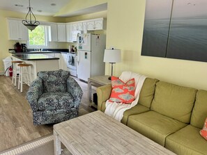 Una sala de estar con un sillón estampado, un sofá verde con almohadones decorativos y una mesa de centro de madera.