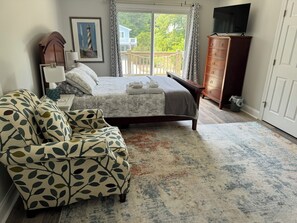 Une chambre avec un lit, une chaise, une commode, un téléviseur et un balcon donnant sur une vue agréable.