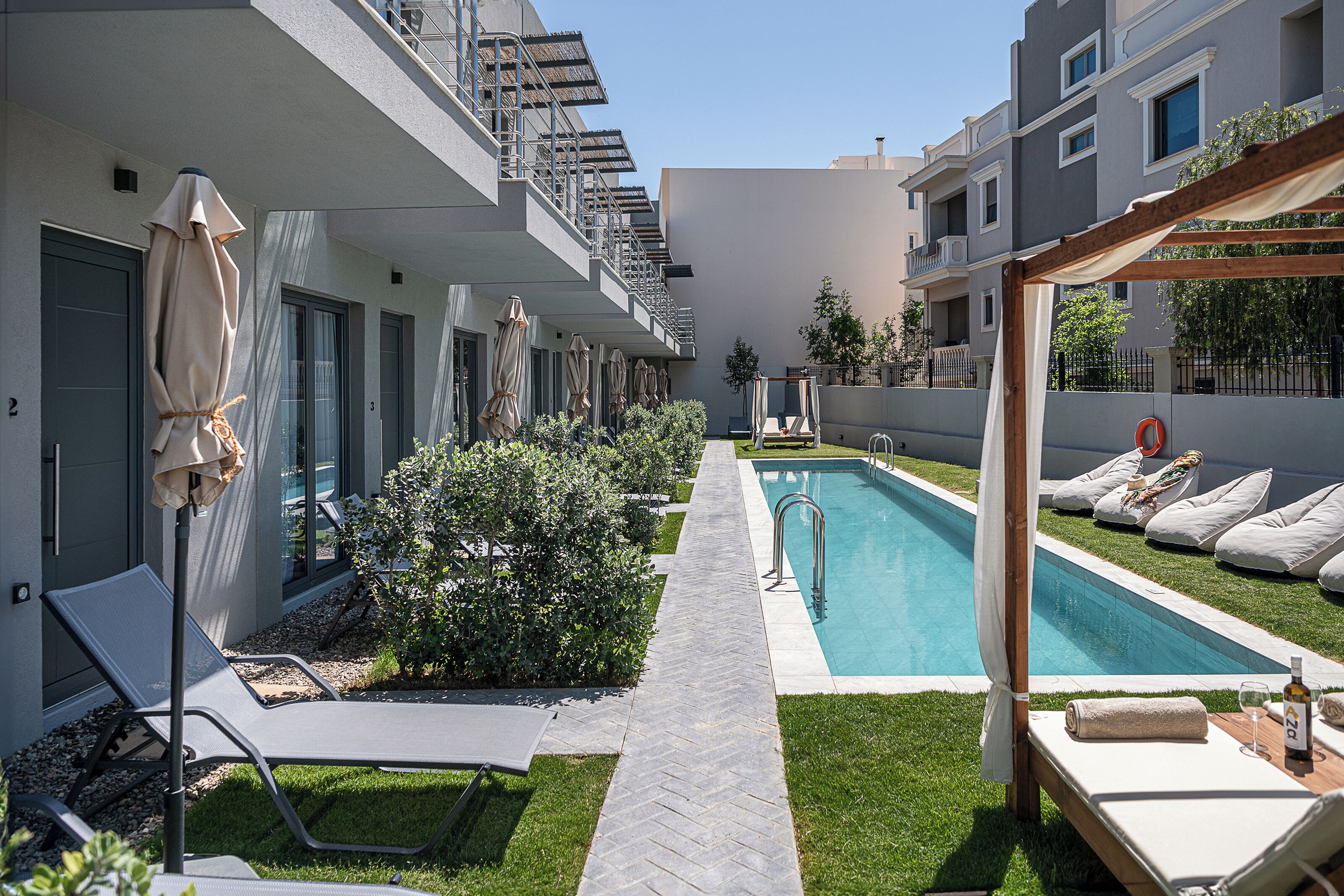 A modern hotel courtyard with a swimming pool, lounge chairs, and a pergola.