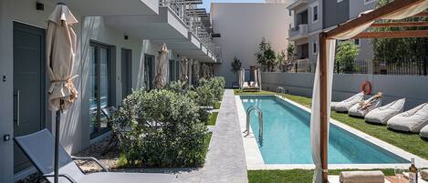 A modern hotel courtyard with a swimming pool, lounge chairs, and a pergola.