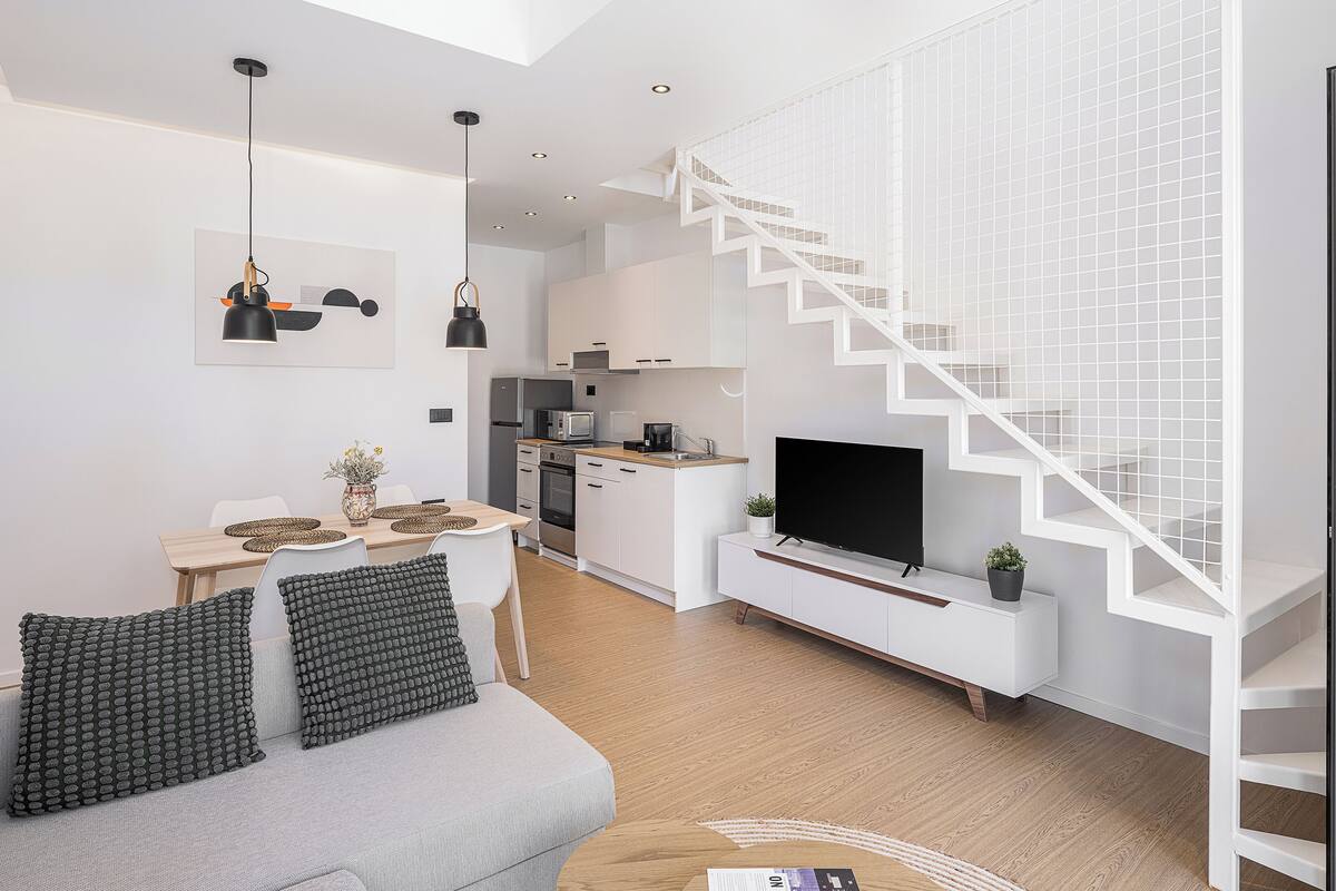 Un espacio habitable moderno con escalera, cocina, comedor y televisión de pantalla plana.