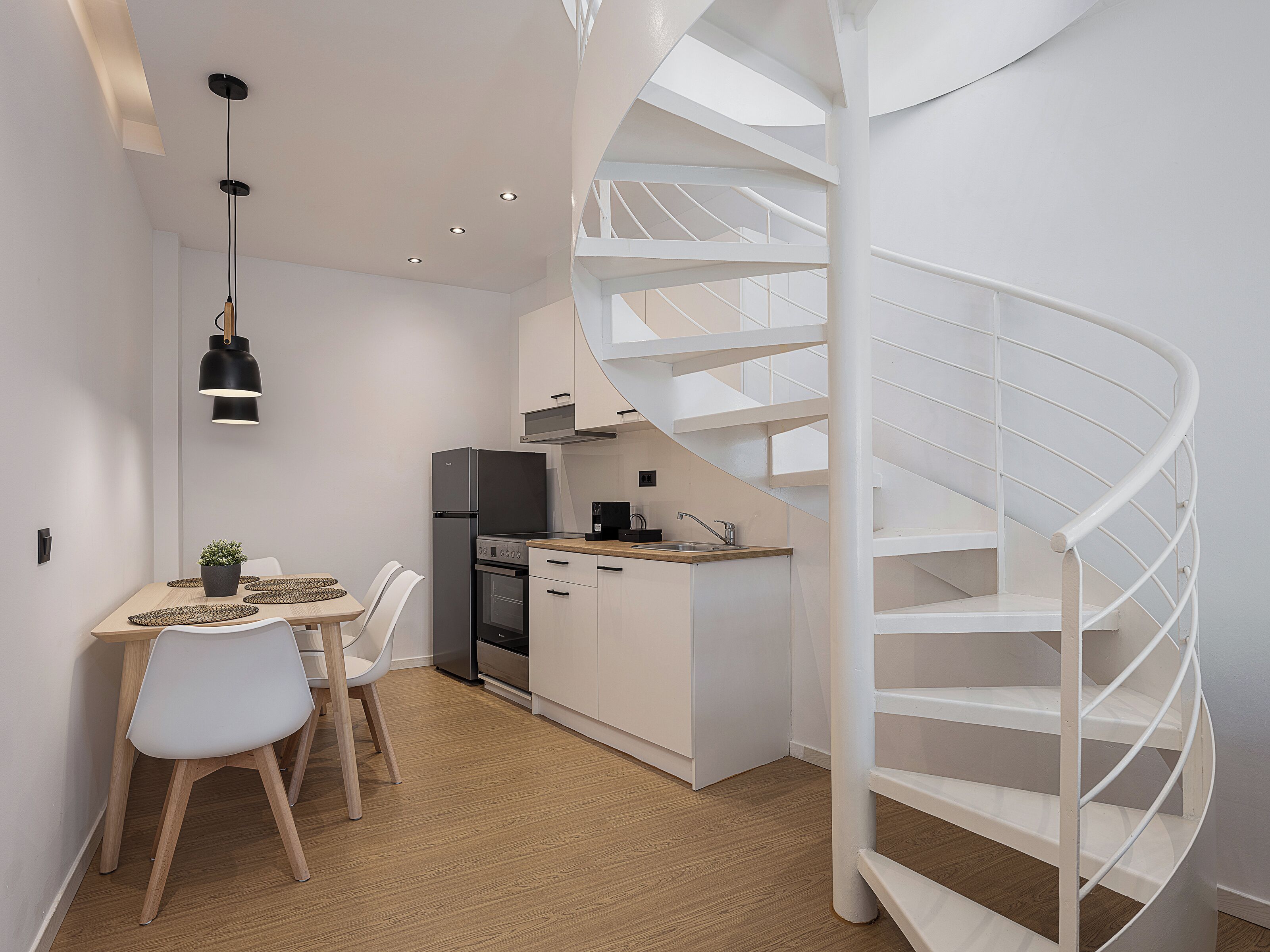 Cozinha moderna com escada em espiral, armários brancos e área de refeições com mesa e cadeiras.