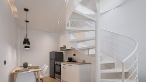 A modern kitchen with a spiral staircase, white cabinetry, and a dining area with a table and chairs. - NEK Suites - Adults Only (Chania)
