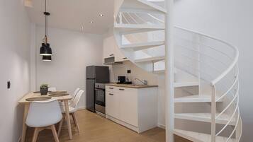Cozinha moderna com escada em espiral, armários brancos e área de refeições com mesa e cadeiras.