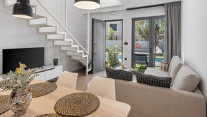 A modern living room with a staircase, a dining area with a vase of flowers, and a view of the outdoors. - NEK Suites - Adults Only (Chania)