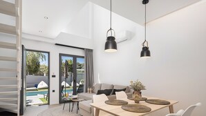 A modern living space with a dining area, a sofa, and a view of an outdoor swimming pool. - NEK Suites - Adults Only (Chania)