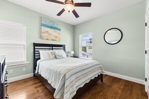 A bedroom with a bed, a ceiling fan, a painting, a window, and a mirror. - 5 Bed, 5 Bath Beach Home/only a 3 Minute Walk To The Beach! Sleeps 12 (Panama City Beach)