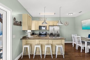 A kitchen with a central island, bar stools, a microwave, a refrigerator, and a dining table with chairs. - 5 Bed, 5 Bath Beach Home/only a 3 Minute Walk To The Beach! Sleeps 12 (Panama City Beach)