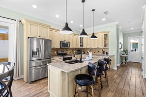 Una cocina moderna con electrodomésticos de acero inoxidable, una isla central con taburetes de bar e iluminación colgante.