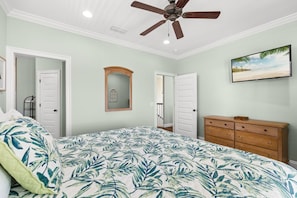 Une chambre à coucher avec un lit, un ventilateur de plafond, une commode et un tableau accroché au mur.