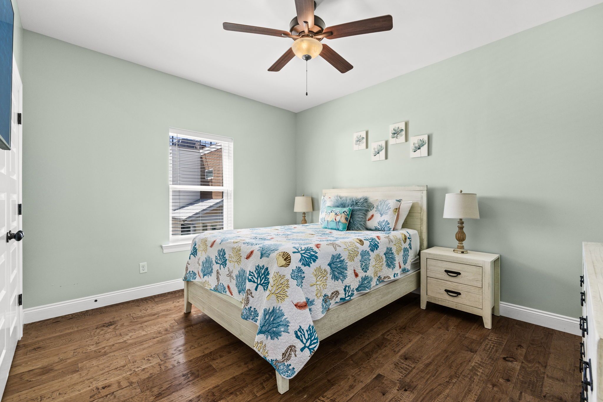 A bedroom with a bed, nightstands, a ceiling fan, a window with blinds, and artwork on the wall.