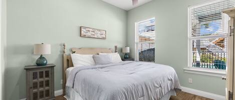 A bedroom with a bed, two bedside tables, a ceiling fan, a window with blinds, and a door.
