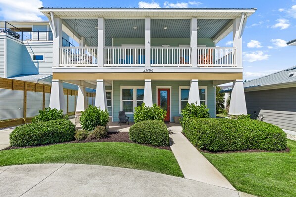 A two-story house with a balcony, a red door, and a well-maintained lawn.