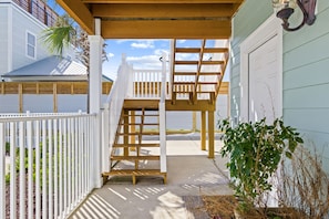 A wooden staircase leading to a covered porch with a white railing, a garage door, and a plant in the foreground. - 5 Bed, 5 Bath Beach Home/only a 3 Minute Walk To The Beach! Sleeps 12 (Panama City Beach)
