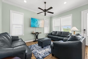 Un salon équipé d’un ventilateur de plafond, d’un téléviseur à écran plat, d’un ensemble de canapés et d’une table basse.