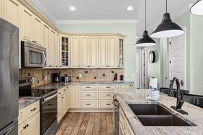 Une cuisine moderne avec des meubles de couleur beige, un réfrigérateur en acier inoxydable, un four à micro-ondes encastré, une machine à café et un évier doté d’un robinet noir.