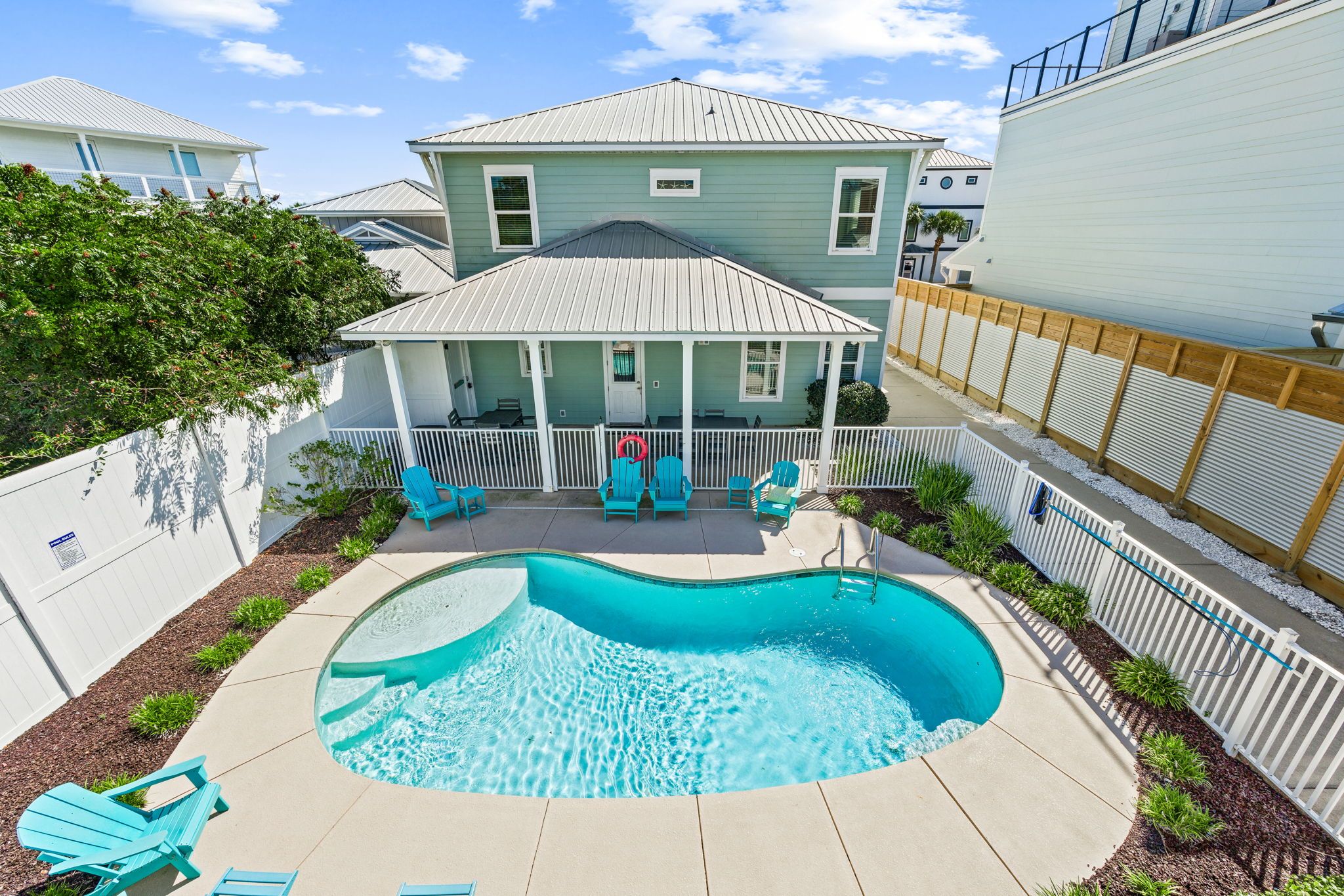 A residential property with a swimming pool, a covered patio with outdoor furniture, and a fenced backyard.