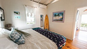 A bedroom with a bed, a surfboard, and a beach-themed painting. - Cayo Loco 1 Bedroom Home (Governor's Harbour)