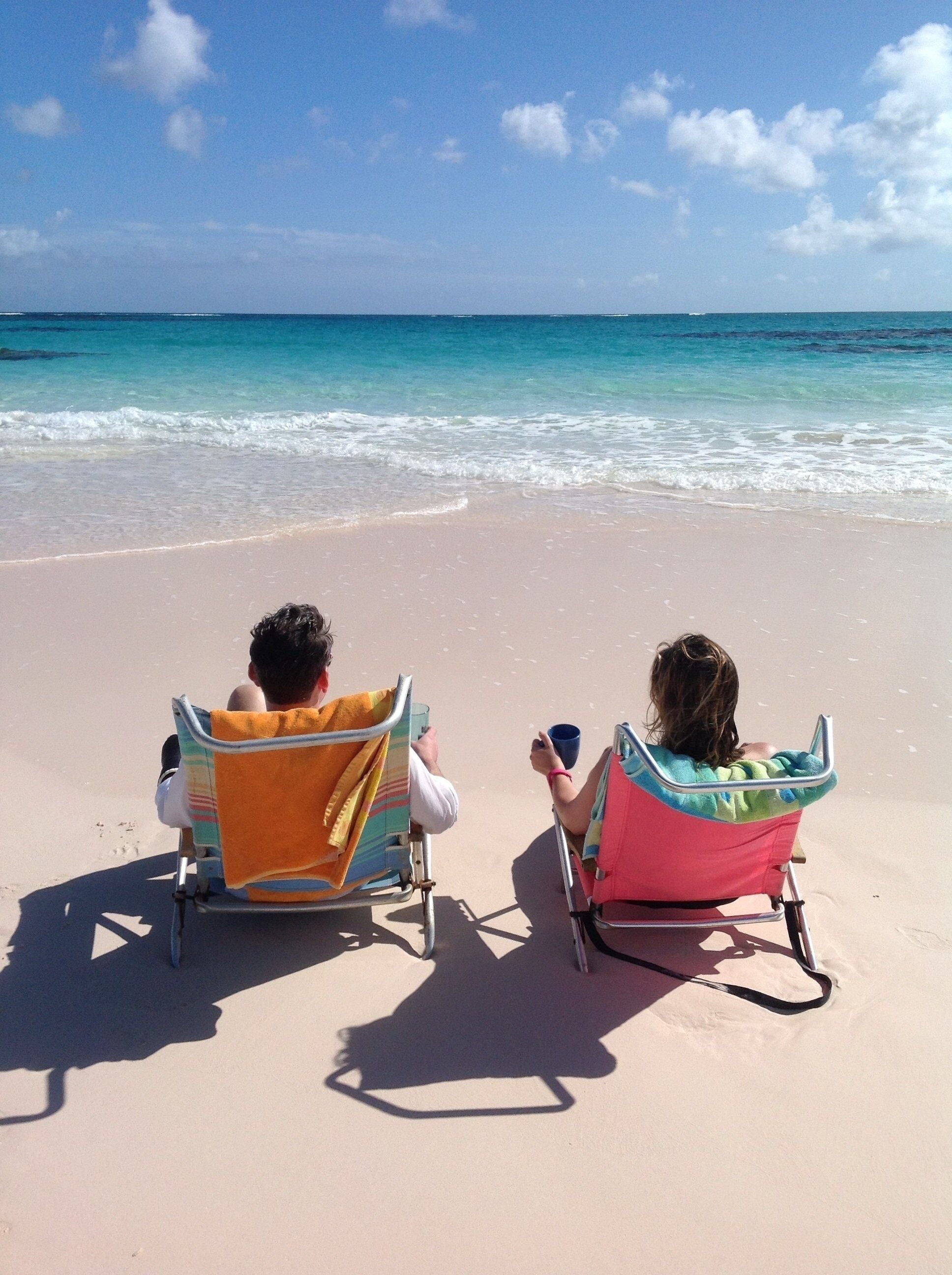 Two beach chairs facing the ocean with towels on them.