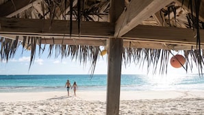 A beach scene with a wooden structure overhead, palm leaves, and a clear view of the ocean. - Cayo Loco 1 Bedroom Home (Governor's Harbour)