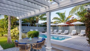 A covered outdoor area with a pool, lounge chairs, and a table with chairs. - One Palm Hill 3 Bedroom Villa (Governor's Harbour)