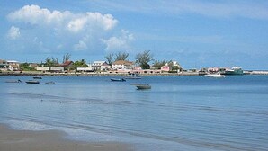 Une plage aux eaux calmes, avec des bateaux et des maisons en arrière-plan.