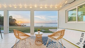 Un espacio de estar al aire libre cubierto con sillas de mimbre y una mesa, con vista a un cuerpo de agua al atardecer.