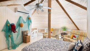 A spacious attic bedroom with a sloped ceiling, a bed with a patterned bedspread, a ceiling fan, and a view of the outdoor balcony area.