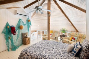 A spacious attic bedroom with a sloped ceiling, a bed with a patterned bedspread, a ceiling fan, and a view of the outdoor balcony area.