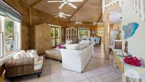 A spacious wooden interior with a high ceiling, multiple ceiling fans, a dining area, and a living room with a sofa and a wicker chair.