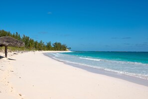 A beach with a thatched hut and a clear blue sky. - Aqua Villa And Cottage 3 Bedroom Home (Governor's Harbour)