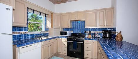 Une cuisine avec des meubles de couleur claire, un crédence en carreaux bleus, une cuisinière, un four à micro-ondes et une fenêtre donnant sur un paysage verdoyant.