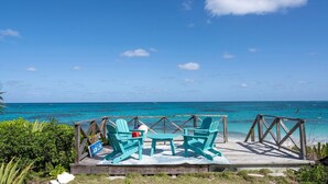 A wooden deck with turquoise Adirondack chairs and a small table, overlooking a turquoise sea under a clear sky. - Aqua Vista 2 Bedroom Home (North Palmetto Point)