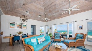 A spacious living room with a large sofa, two armchairs, a dining table, and a view of the ocean. - Aqua Vista 2 Bedroom Home (North Palmetto Point)