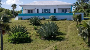 A two-story building with a flat roof, surrounded by a well-maintained lawn and various tropical plants. - Aqua Vista 2 Bedroom Home (North Palmetto Point)