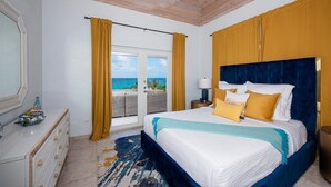 A bedroom with a large bed, a dresser, a mirror, and a view of the ocean. - Aqua Vista 2 Bedroom Home (North Palmetto Point)