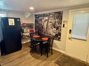 Una cocina compacta con refrigerador, una mesa de comedor con sillas y un cartel con vista a la ciudad en la pared.