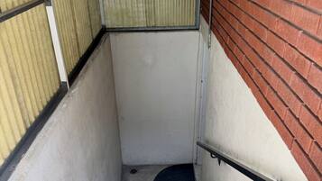 Un escalier en béton avec une rampe métallique, menant à une porte dotée d’un cadre métallique, avec un mur blanc d’un côté et un mur en briques rouges de l’autre.