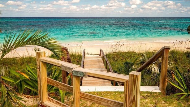 Un escalier en bois mène à une plage d’où l’on a une vue dégagée sur l’océan.