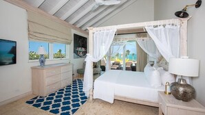 Une chambre à coucher avec un lit à baldaquin, un ventilateur de plafond, une télévision, une commode et une vue sur l’extérieur.