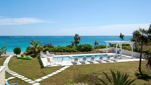 A pool area with lounge chairs and a cabana, overlooking a beach with palm trees and the ocean. - Endless Summer 5 Bedroom Home (Double Bay)