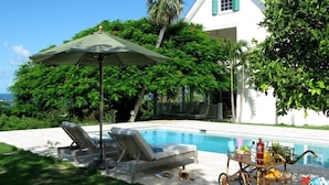 A poolside area with lounge chairs, a table with drinks, and a house in the background. - Buccaneer Hill Cottage 1 Bedroom Cottage (Governor's Harbour)