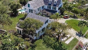A large house with a stone roof, surrounded by lush greenery and a view of the ocean. - Buccaneer Hill Cottage 1 Bedroom Cottage (Governor's Harbour)
