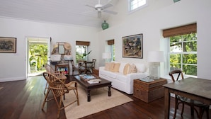 A spacious living room with a white sofa, wicker furniture, and a dining area with a table and chairs. - Buccaneer Hill Cottage 1 Bedroom Cottage (Governor's Harbour)