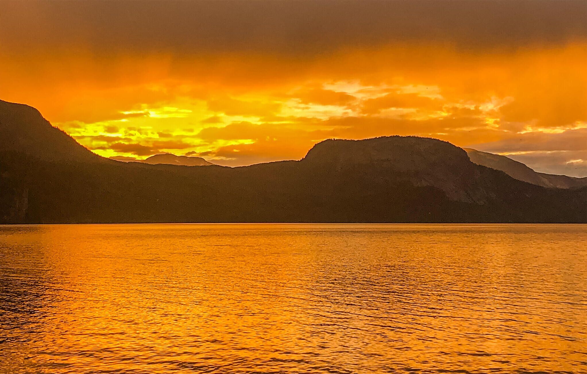 A calm lake reflecting a sunset with mountains in the background.
