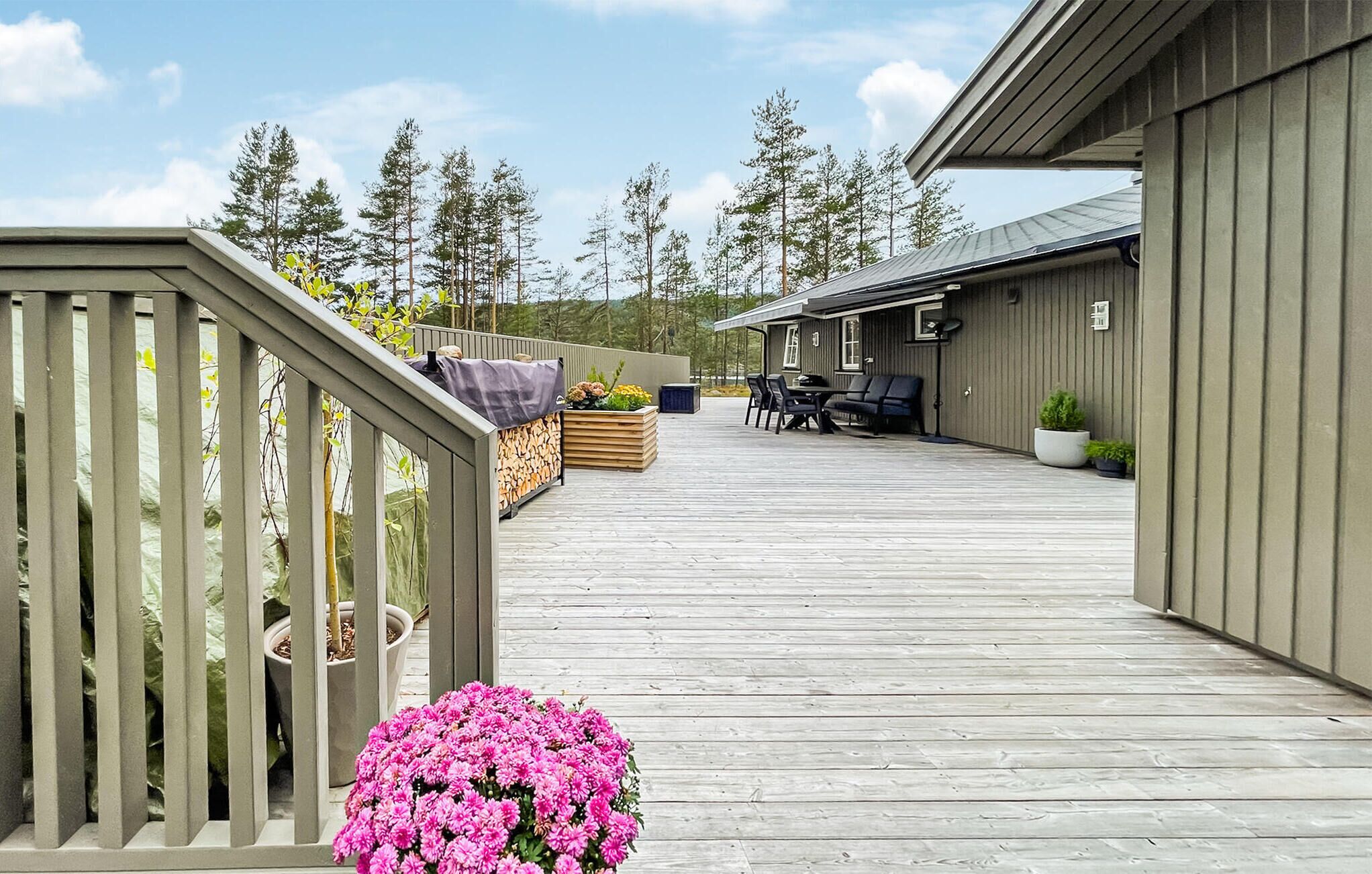 A wooden deck with a railing, a seating area with a table and chairs, and a building with a sloped roof.