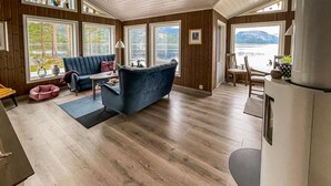 Ein gemütliches Blockhaus-Interieur mit einem blauen Sofa, Holzboden und großen Fenstern mit Seeblick.