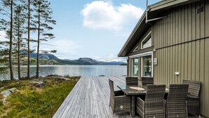 Eine Holzterrasse mit Gartenmöbeln mit Blick auf einen See und Berge.