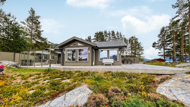 A modern cabin with a large glass door, a deck, and a view of the surrounding forest. - Cozy home in Nissedal with house sea view (Nissedal)