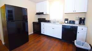 A compact kitchen with white cabinets, a black refrigerator, a stove, a dishwasher, and a coffee maker. - Bayshore Drive 211 3 Bedroom Home by RedAwning (Ocean City)